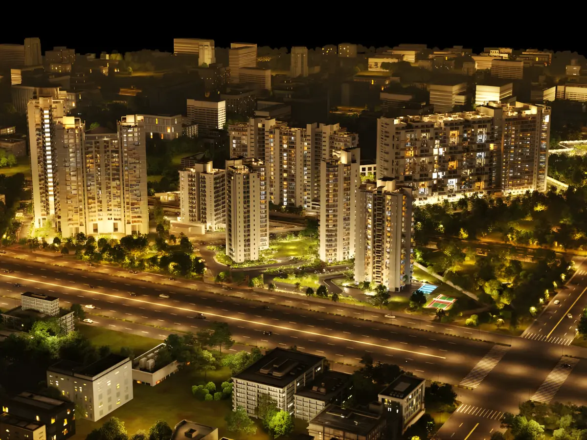 An aerial night view showcases brightly lit modern residential towers in Gurgaon, with a multi-lane highway bustling with car lights in the foreground, and illuminated trees and smaller buildings scattered throughout the urban landscape.