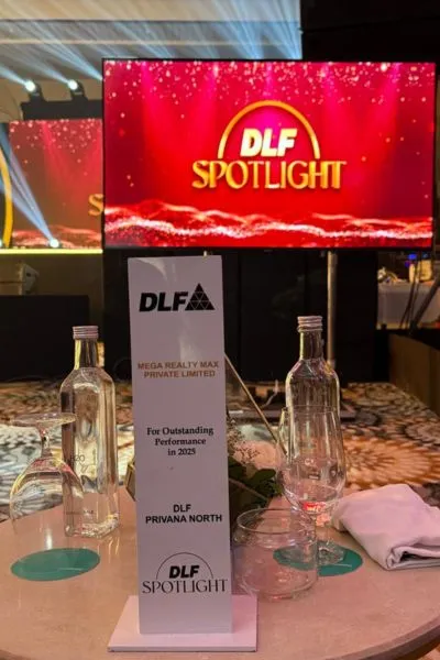 A trophy/standee award from DLF presented to Mega Realty Max Private Limited for Outstanding Performance in 2025 for DLF Privana North, placed on a table at the DLF Spotlight event with a red LED screen in the background displaying the DLF Spotlight branding.