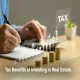 Person writing notes with stacked gold coins and a glowing TAX growth chart on a desk representing tax benefits of investing in real estate.