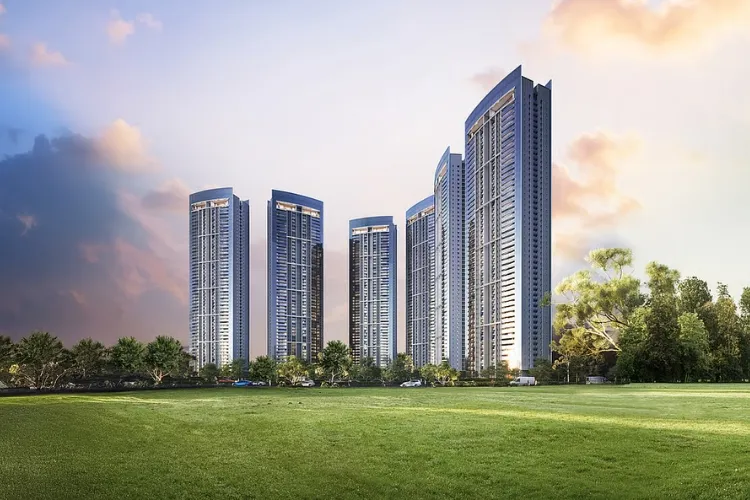 Panoramic view of the modern high-rise residential towers of DLF Privana South, set against a vibrant sky with a vast green lawn and lush trees in the foreground, showcasing luxury living in Gurugram.
