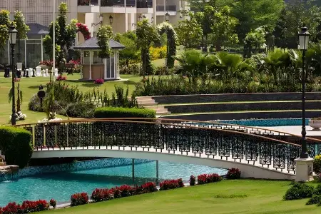 Central Park 104 – Garden Serenity with Canal Bridge in Gurugram’s Luxury Enclave Daylight view of Central Park 104 Gurugram featuring a decorative bridge over turquoise canal, manicured gardens, flower beds, and palm trees