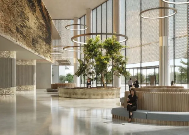 Landmark One Double-Height Lobby Atrium with Greenery Double-height lobby atrium at Landmark One with a large potted tree at the center, circular ring pendant lights hanging above, woven textured wall panels, floor-to-ceiling glass walls, and a woman seated on a wooden bench.