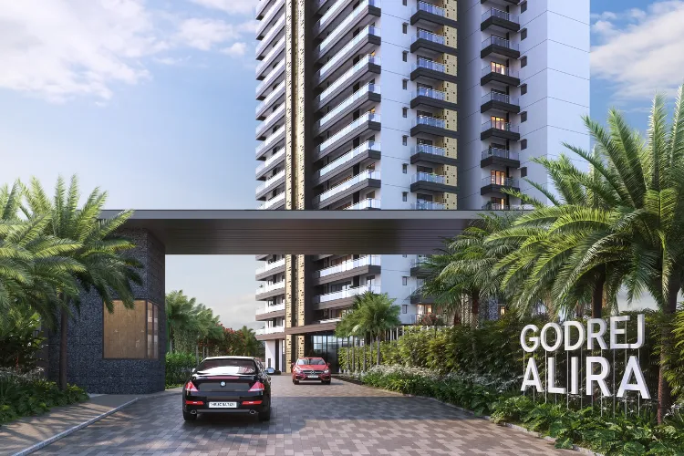 The grand entrance of Godrej Alira in Sector 39, Gurugram, featuring a modern architectural gate, lush palm trees, and the property's name. A car is visible on the driveway.