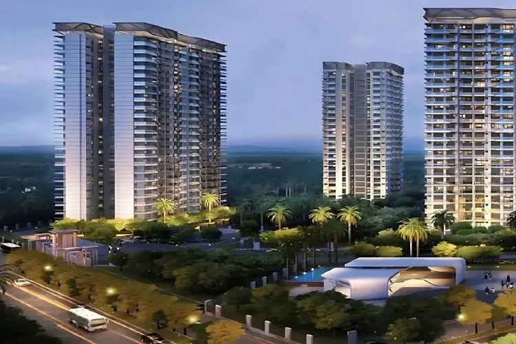A digital rendering of Godrej Meridian, a residential complex featuring three modern high-rise towers with extensive glass facades, set amidst landscaped greenery and a swimming pool, with a road and other low-rise buildings in the foreground. The image has a soft, twilight feel.