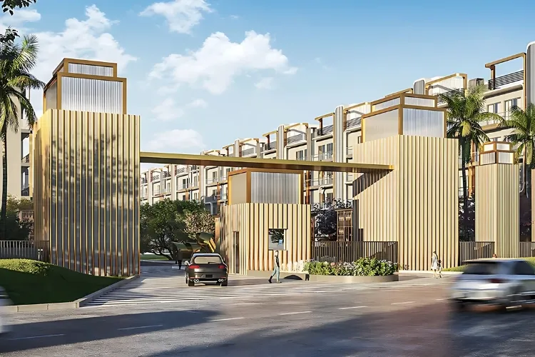 The grand entrance to M3M Antalya Hills in Gurugram, featuring modern architectural structures with golden vertical louvers, a prominent overhead beam, lush landscaping including palm trees, and vehicles entering and exiting under a clear sky.