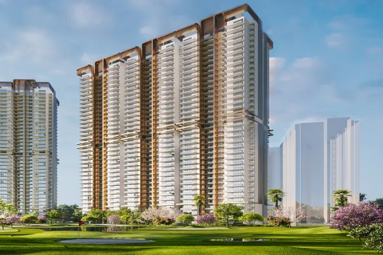  A digital rendering of M3M Capital, a modern residential complex in Gurgaon. The image shows a tall, elegant tower with numerous balconies and a distinctive architectural top, standing next to a similar, partially visible building. The foreground features a lush green lawn, trees with pink and white blossoms, and a red flag on a golf course, all under a clear blue sky.