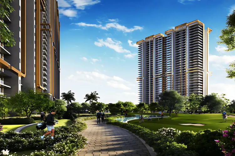  A bright, daytime architectural rendering of the M3M Mansion residential complex. The image shows two modern high-rise towers flanking a meticulously landscaped central park area with walking paths, lush green grass, trees, and a water feature. Several people are depicted strolling or playing golf in the recreational space, set against a vibrant blue sky with scattered clouds.