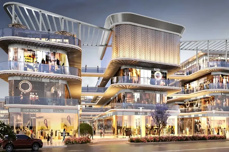 Wide, eye-level rendering of M3M Route 65, showcasing its multi-level, modern architecture with curved glass facades. The complex is brightly lit at dusk, highlighting numerous retail storefronts with visible luxury brand names like Louis Vuitton, Calvin Klein, BOSS, and Parda. Pedestrians are seen strolling on walkways, and a car is parked on the street in the foreground, indicating a bustling commercial environment.