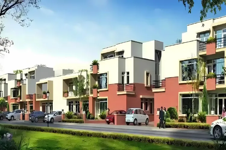 An aerial view of the Nirvana Country residential township in Gurugram. The image displays a well-planned, sprawling community with a mix of modern low-rise villas and mid-rise apartment buildings. The township is characterized by its abundant green spaces, including lush, landscaped gardens, parks, and tree-lined streets. A clubhouse, a swimming pool, and other recreational amenities are visible, highlighting the luxurious lifestyle within the gated community.