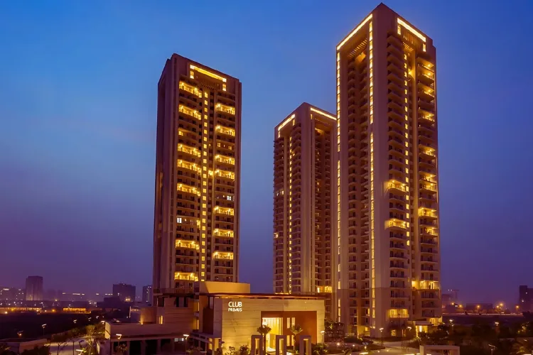 Three modern high-rise residential towers of DLF The Primus are illuminated with warm lights against a deep blue twilight sky, showcasing the 