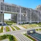 A wide-angle photo of the ultra-luxury residential towers at DLF The Dahlias, showcasing their unique white architectural facade and a prominent sky bridge. The foreground features meticulously landscaped gardens, including colorful flower beds and paved walkways leading to the building entrance on Golf Course Road, Gurugram.