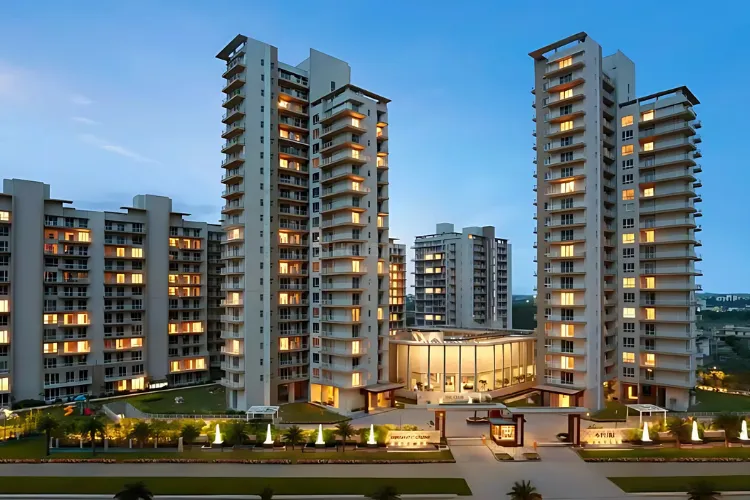  A beautiful twilight photo of the Puri Diplomatic Residences. The image shows a cluster of modern high-rise residential towers, with many windows and balconies softly lit from within. The central building features a contemporary glass facade for its entrance and lobby. The complex is surrounded by manicured lawns and subtle, warm lighting along the pathways, set against a calm blue evening sky.