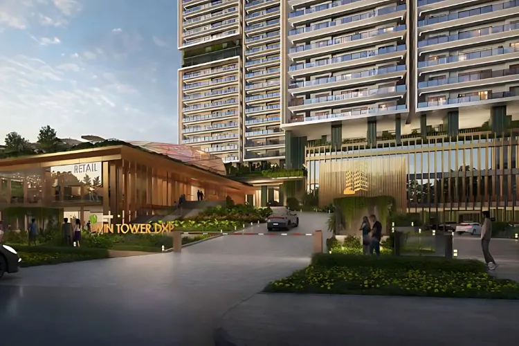 A daytime view of the main entrance to Signature Global Twin Tower DXP in Gurugram, Haryana, showing the multi-story retail block on the left with the residential towers visible behind. Cars are entering through a boom barrier, and people are walking around the landscaped pathways.